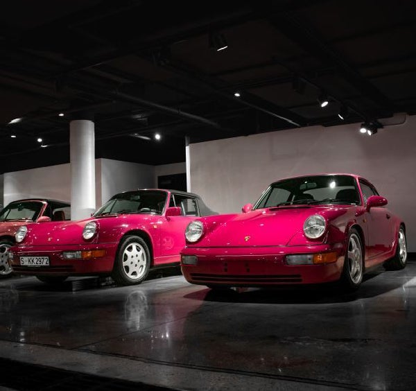 Three vibrant magenta Porsche 911s in a modern showroom with dark floors and white walls.