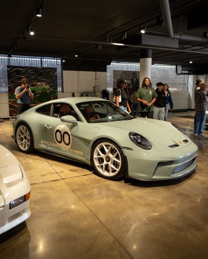 A light green Porsche sports car sits in a modern showroom as people view the vehicle.
