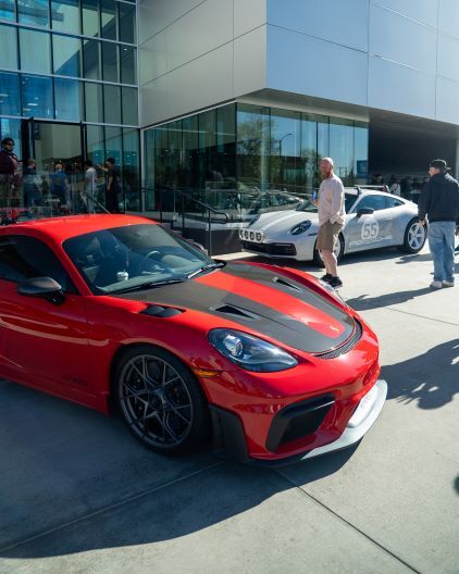 A red and black sports car stands in front of a modern building as people observe it.