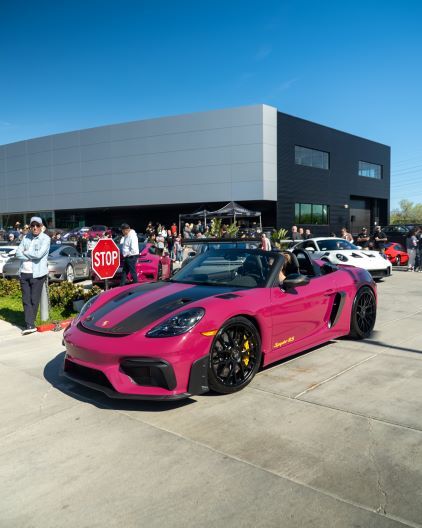 A bright pink Porsche 718 Spyder RS convertible sits parked in front of a modern building.