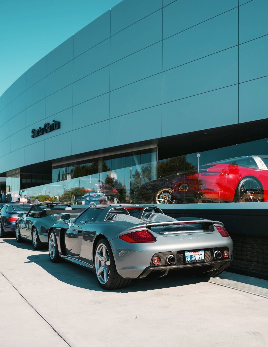 A silver Porsche Carrera GT parked in front of a modern dealership building with other sports cars.