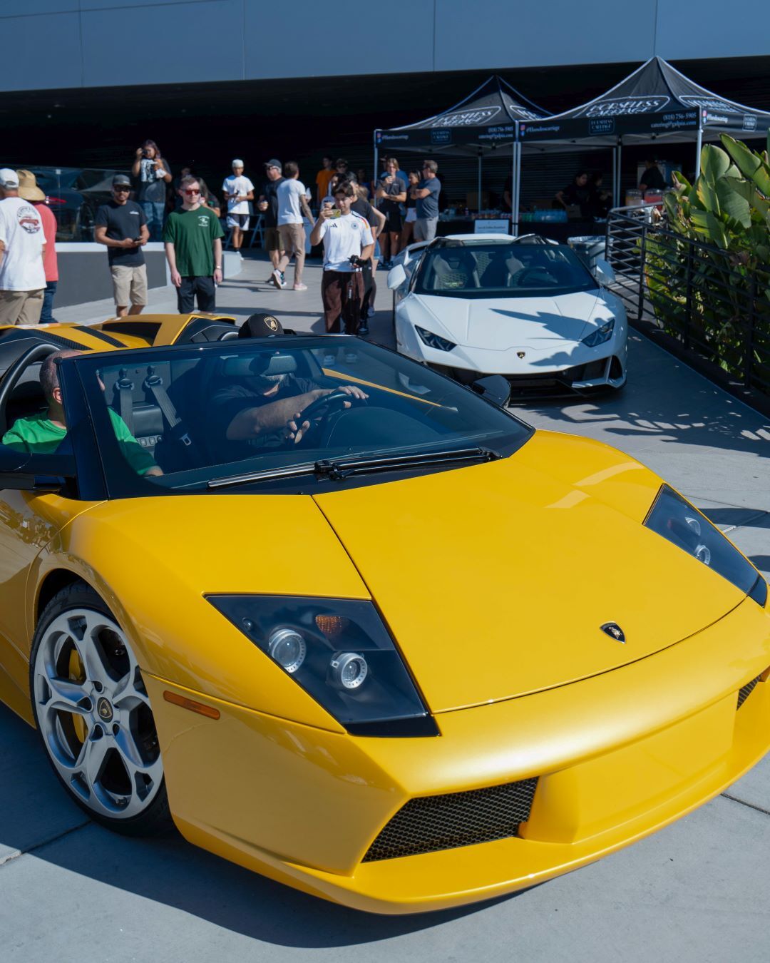 A bright yellow Lamborghini Murcielago convertible with men standing around it and a white Lamborghini behind it.