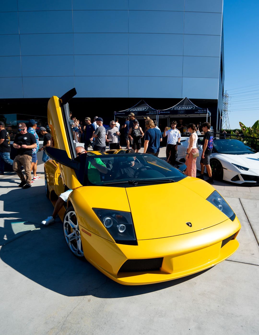 Bright yellow Lamborghini with a raised scissor door, parked among a crowd of people at an outdoor car show.