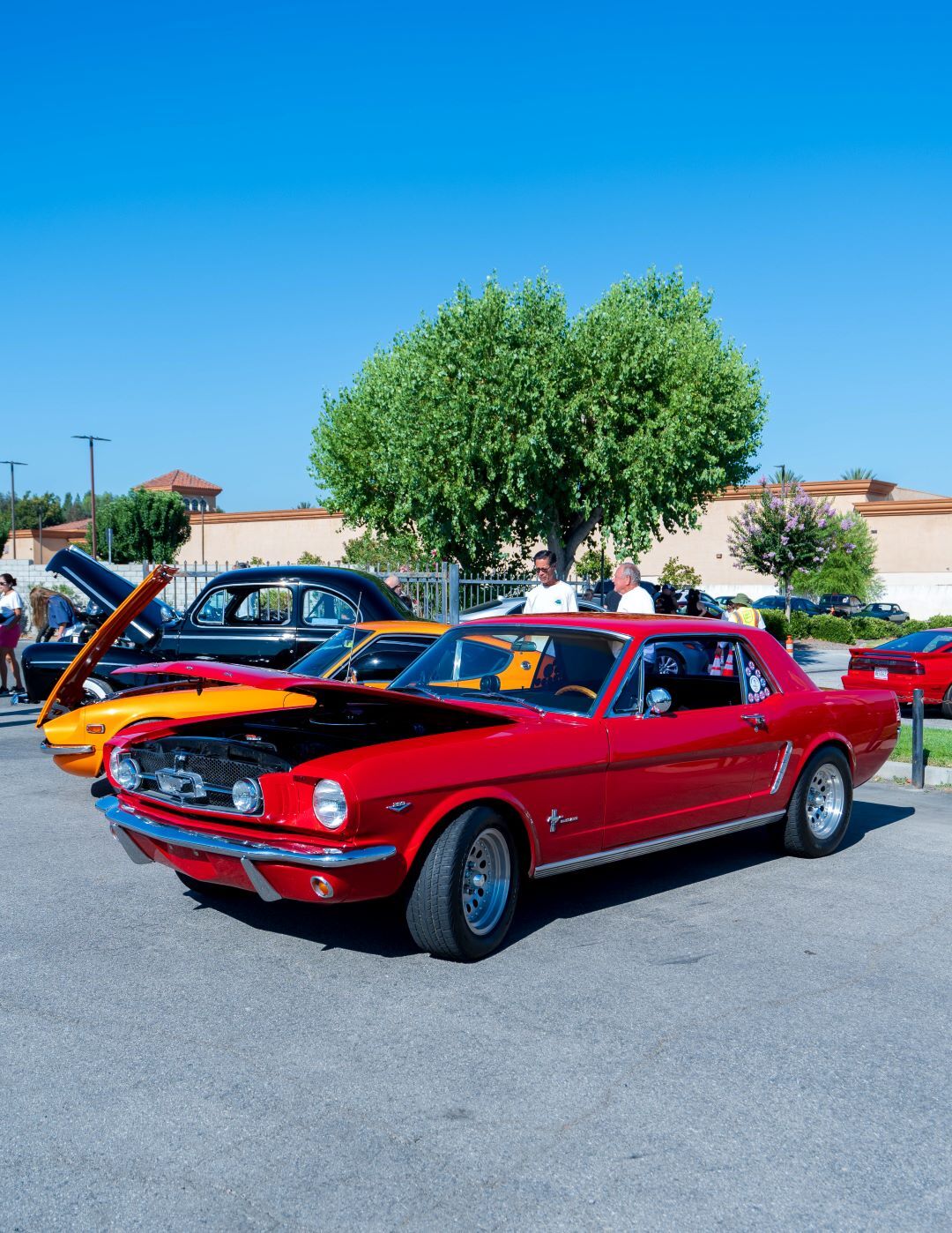 A meticulously restored red 1960s Ford Mustang parked at a car show on a sunny day.