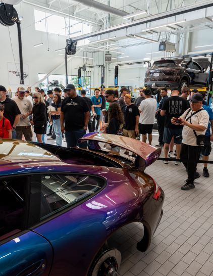 A crowd gathers at an automotive event, admiring custom cars and vehicles on lifts.