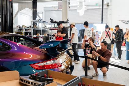 People examine a sleek, dark red and blue sports car at an auto show.