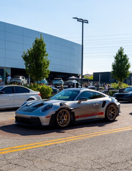 A silver Porsche 911 GT3 parked on a street at a car show with onlookers.