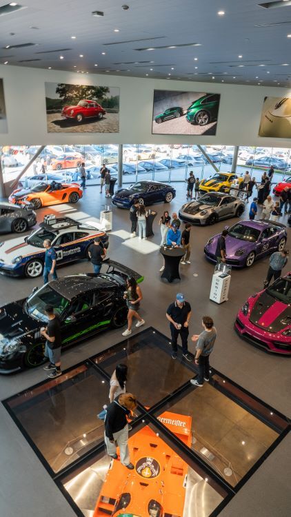 People mingle among luxury Porsche cars displayed in a modern, upscale showroom.