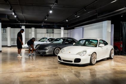 Two people examine a white Porsche sports car in a modern, well-lit showroom.
