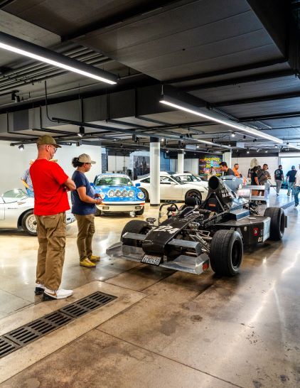 Two men in hats observe a black race car on a trailer in a car showroom.