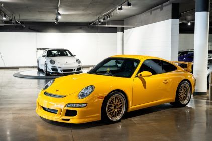 A yellow Porsche 911 sits on a circular platform in a modern showroom.