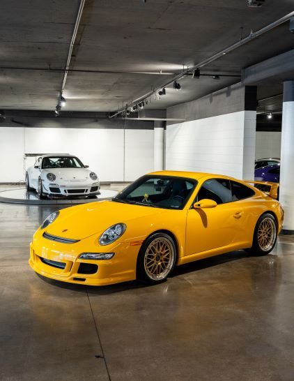 A bright yellow Porsche sits on a rotating platform in a modern, concrete garage.