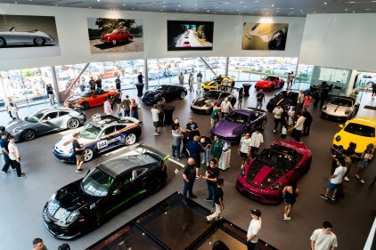 Multiple luxury cars are displayed in a large, modern showroom as people browse around.
