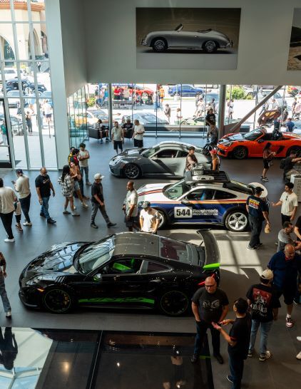 Several luxury cars are displayed in a modern showroom with people viewing them.