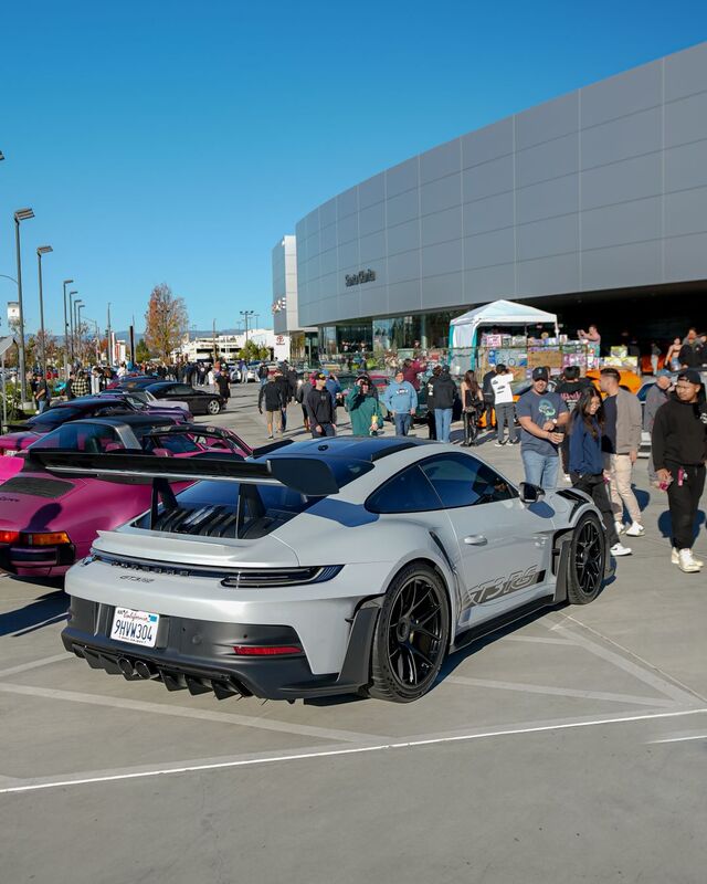 A gray Porsche 911 GT3 RS sits on display at a car show with a crowd of onlookers.