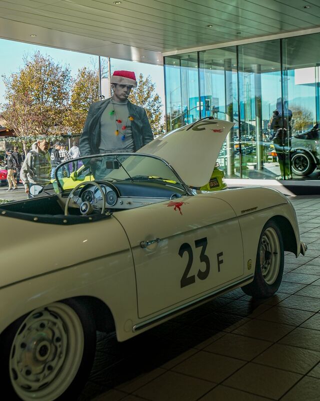 A vintage white Porsche 356 convertible sits on display with its hood open, and a Santa Claus cutout is visible through the window behind it.