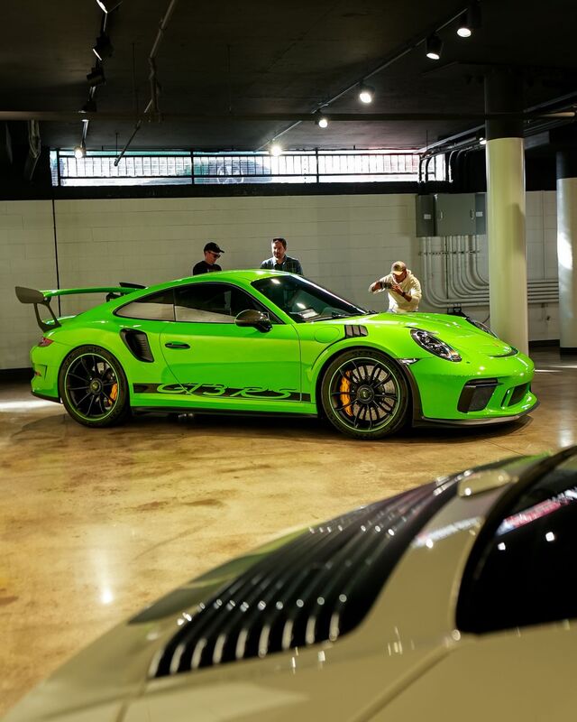 A bright green Porsche 911 GT3 is parked indoors as people observe it.