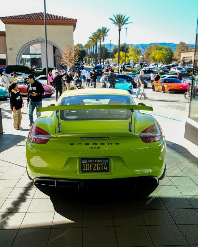 A bright green Porsche GT4 sits parked among other cars at a car meet.