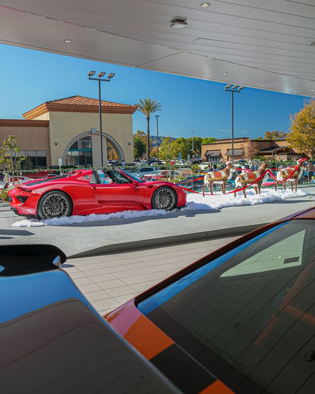 A red convertible sits on a snowy display next to reindeer decorations in a parking garage.