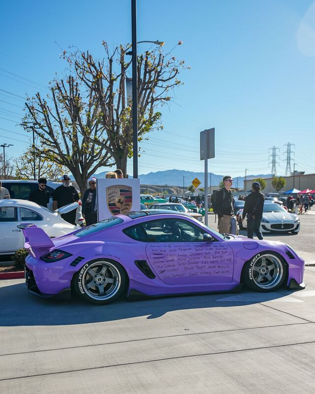 A purple modified car sits at a car show with onlookers admiring it.
