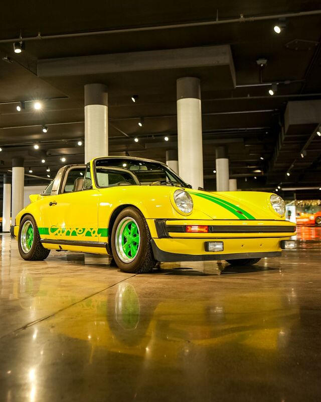 A yellow Porsche Carrera with green stripes and wheels sits in a spacious, well-lit garage.