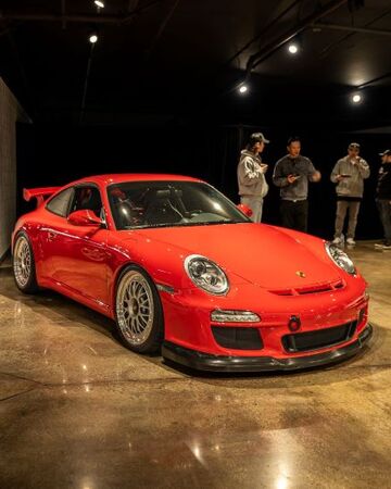 A red Porsche sports car sits on display while several people nearby observe it.