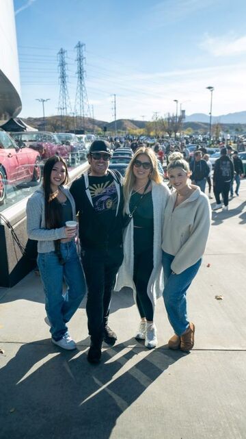 Four people pose for a photo outdoors with a parking lot and power lines in the background.