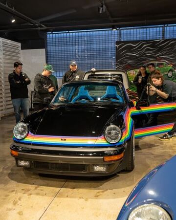 A black Porsche with colorful rainbow stripes stands center, while people observe nearby.