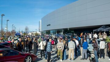 A large crowd gathers outside a modern building on a sunny day.