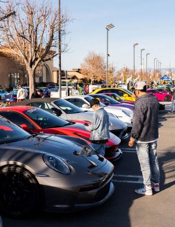 Several people admire a row of brightly colored luxury cars at an outdoor car show.