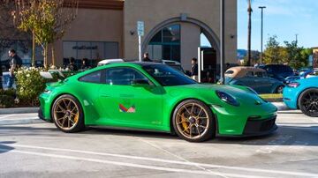 A bright green Porsche car sits in a parking lot with other vehicles nearby.