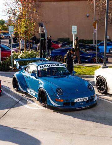 A blue Porsche with a large spoiler is displayed at a car show, with spectators observing nearby.