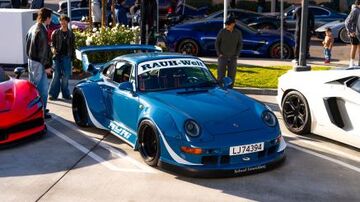 Several people admire a blue Porsche 911 with custom modifications at a car show.