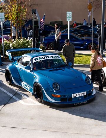 A modified blue Porsche 911 sits on display with people observing and taking photos nearby.
