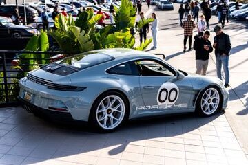 A gray Porsche sports car with white wheels and '00' decals is parked on a sidewalk.