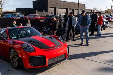 A red sports car sits in a parking lot as a group of people admire it.