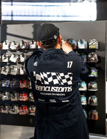 A person in a racing jumpsuit reaches for a product on a shelf filled with merchandise.