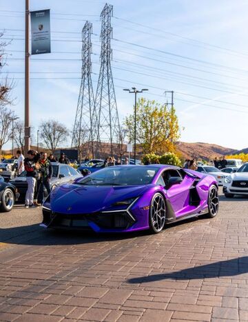 A purple Lamborghini Aventador sits parked at a car show with onlookers nearby.