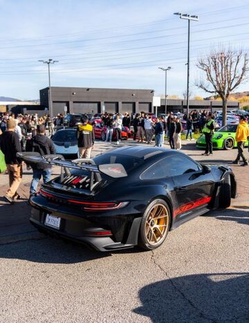 A black Porsche 911 with a large rear wing sits parked at a car show surrounded by spectators.