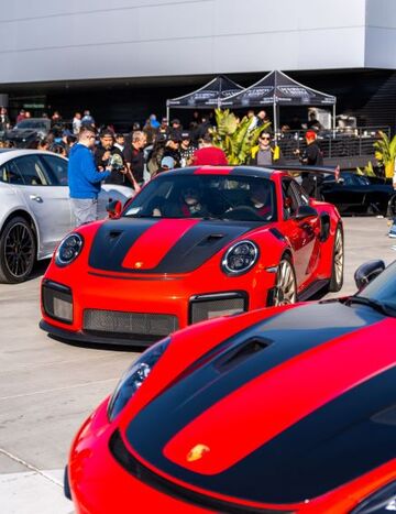 A red Porsche 911 GT3 is on display as a crowd of people take photos of it.