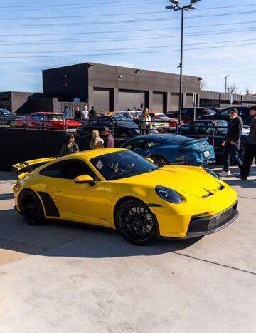 A bright yellow Porsche sits parked among other luxury cars at an outdoor car show.