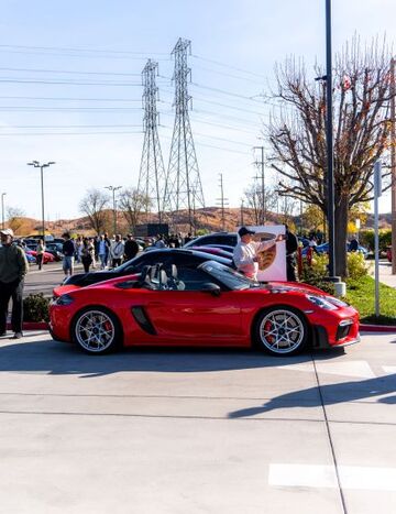 A person in a red shirt poses next to a shiny red sports car at an outdoor event.