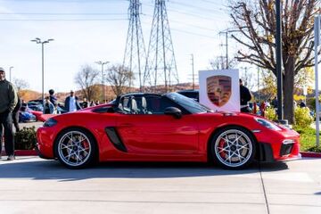 A red Porsche convertible is on display with a framed portrait resting on its hood at an outdoor car show.
