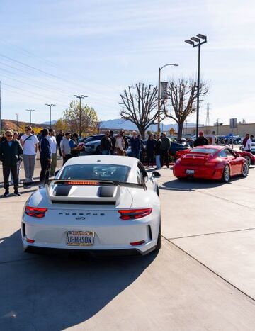 A red Porsche and a white Porsche sit on display as a crowd of people observe the vehicles.