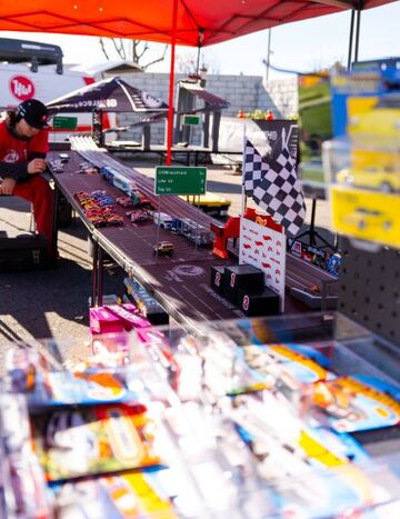 A man operates a slot car racetrack with colorful cars competing under a red and white canopy.