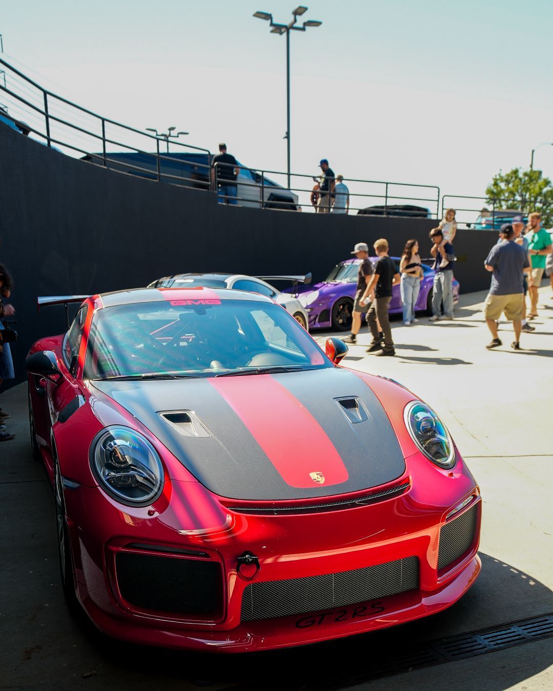 Red Porsche GT2RS with a black and red striped hood, parked with other cars and people admiring them.