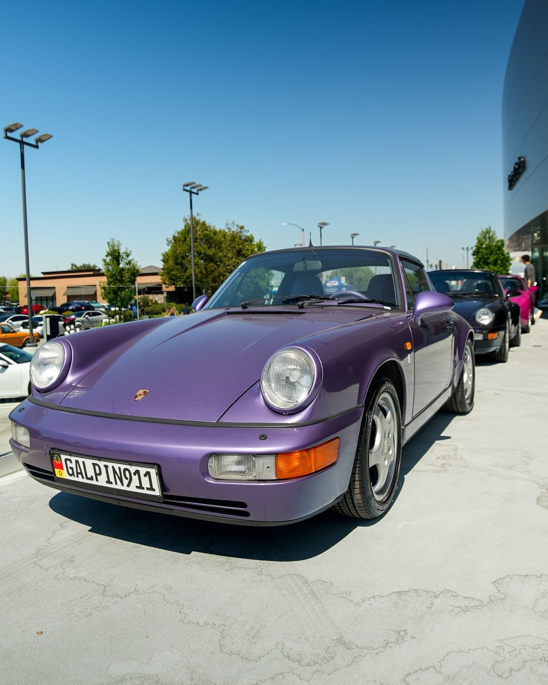 A shiny purple vintage Porsche 911 convertible parked in a line of similar cars under a clear blue sky.