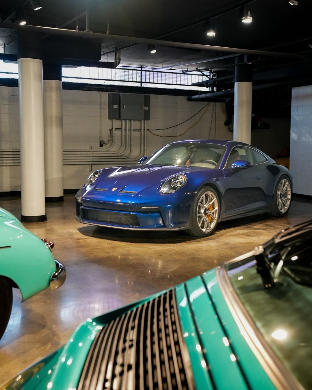 A vibrant blue sports car with orange brake calipers and bright headlights, parked among other teal cars.