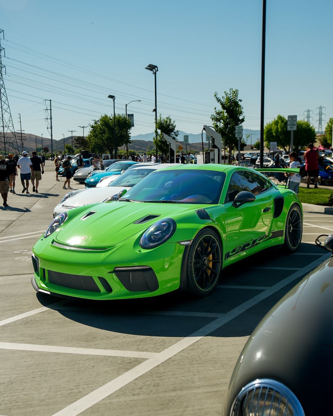 A bright green Porsche 911 GT3 RS parked in a lot, with other cars and people in the background.