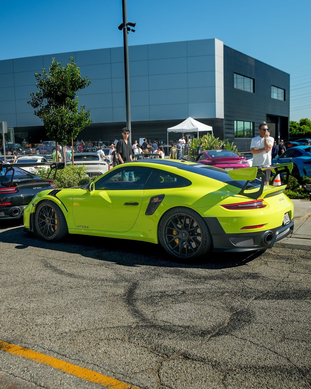 Bright green Porsche 911 GT2 RS parked on asphalt with burnout marks, people beside a modern building.
